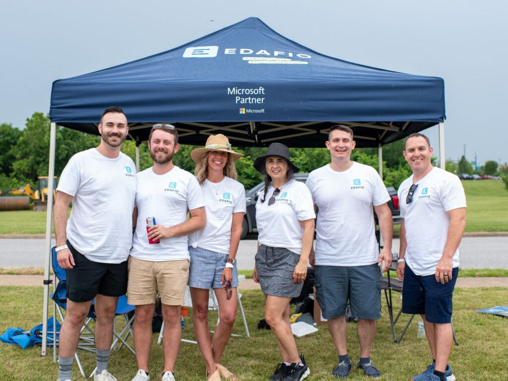 Edafio employees in casual wear standing in front of a tent with the Edafio logo and the words Microsoft Partner.