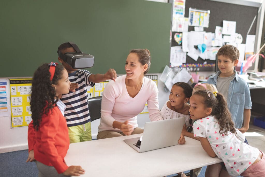 Teacher with elementary students gathered around, one wearing a VR headset